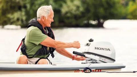 Monsieur sur un bateau démarrant un moteur Honda BF5.